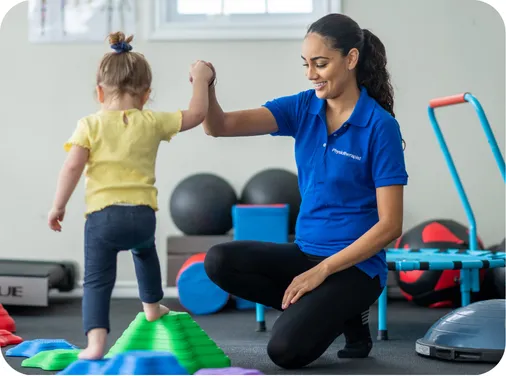 Woman supporting a child during a physiotherapy session in a home setting.