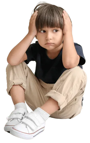 Young boy in a white shirt sitting on the floor with knees folded, holding his head