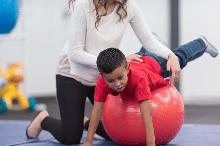 A child receiving physiotherapy while balancing on a therapy ball. autism spectrum disorder