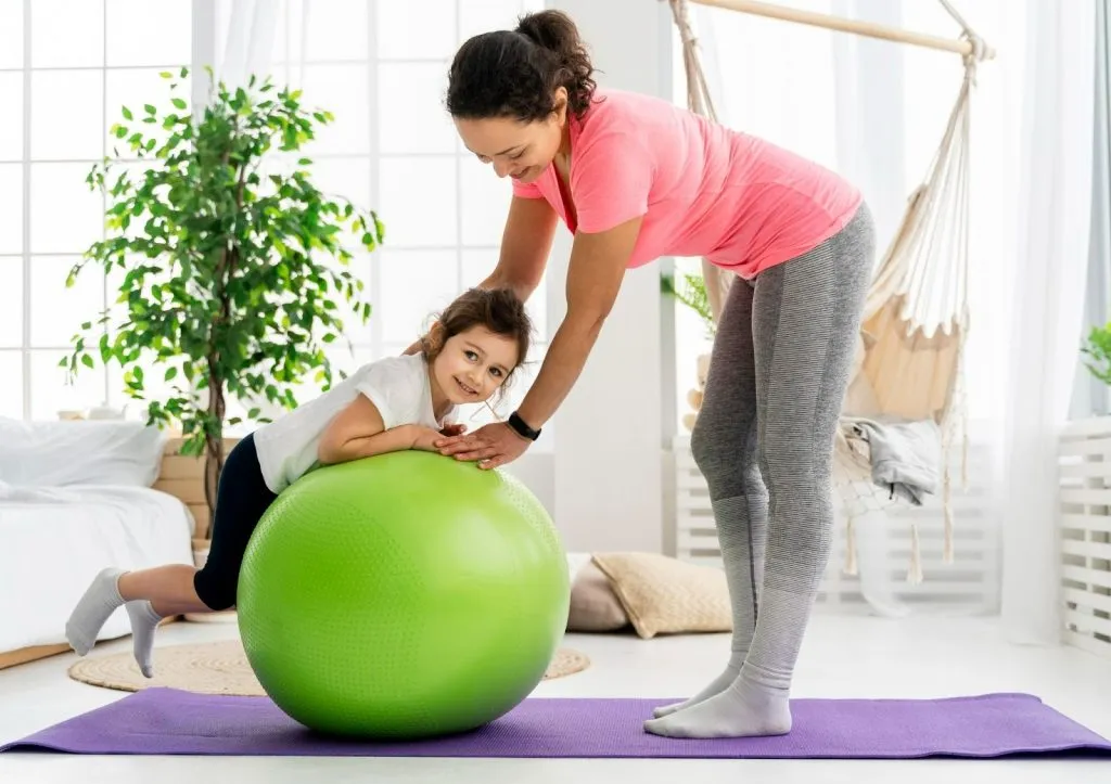 Paediatric physiotherapist helping a child balance on a gym ball during home visit physio in Sydney