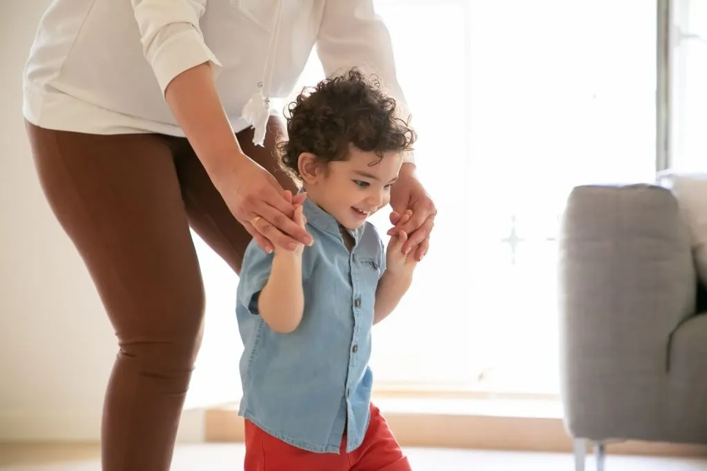 Parent helping young boy practise walking at home during physiotherapy funded by the NDIS for children