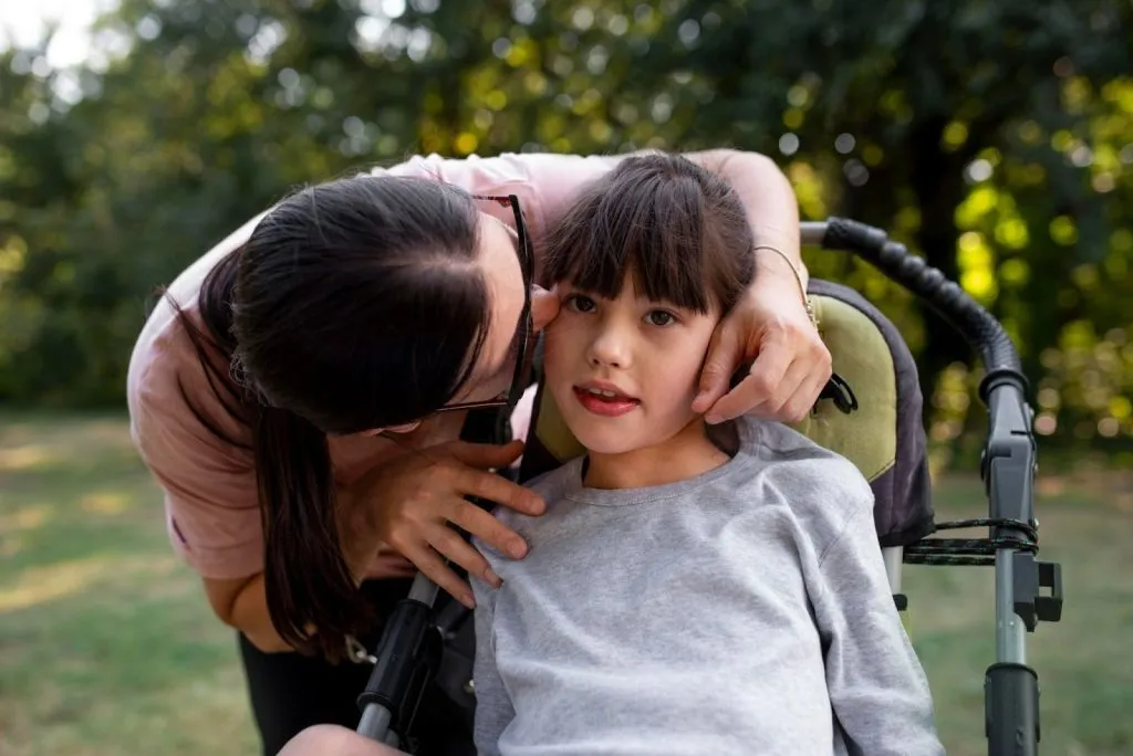 Mother comforting her child in a wheelchair outdoors, symbolising family support under the NDIS for children program