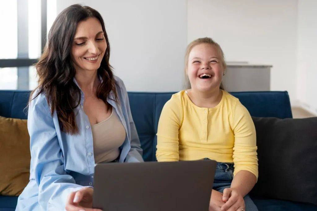 Therapist working with smiling girl using a laptop in a therapy session supported by the NDIS for children